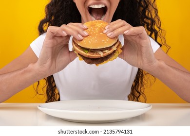 Close Up Of Funny Hungry Lady Biting Burger Eating Junk Food Over Plate Posing With Open Mouth, Yellow Orange Studio Wall. Woman Enjoying Hamburger. Unhealthy Nutrition And Binge Eating Habit Concept