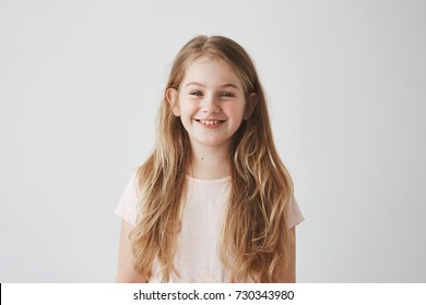Close up of funny little girl with blue eyes and blonde hair laughing,looking in camera with satisfied expression, posing for family photo.