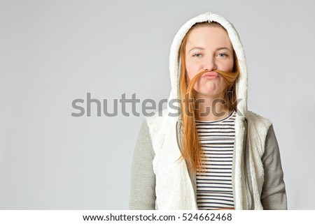 Close up funny young caucasian woman in hoody putting her hair between nose and lip like moustache. Copy space at the side.