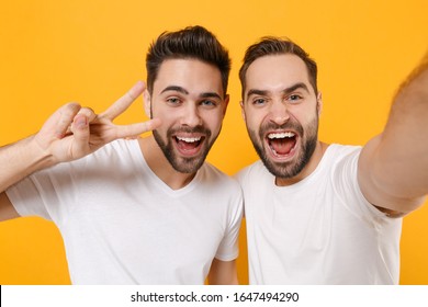 Close up of funny young men guys friends in white t-shirts isolated on yellow orange background. People lifestyle concept. Mock up copy space. Doing selfie shot on mobile phone showing victory sign - Shutterstock ID 1647494290