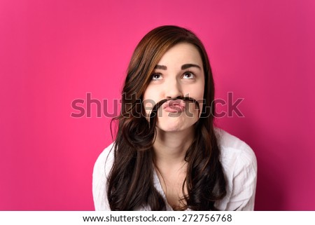 Close up Funny Young Woman Putting her Hair Between Nose and Lip and Looking Up. Isolated on a Pink Background.