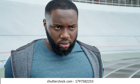 Close Up Of Furious Afro Man Starting To Run On Modern Track. Portrait Of Emotional Runner Jogging On Racetrack In Slow Motion. Young Guy Exercising At Stadium Track Alone