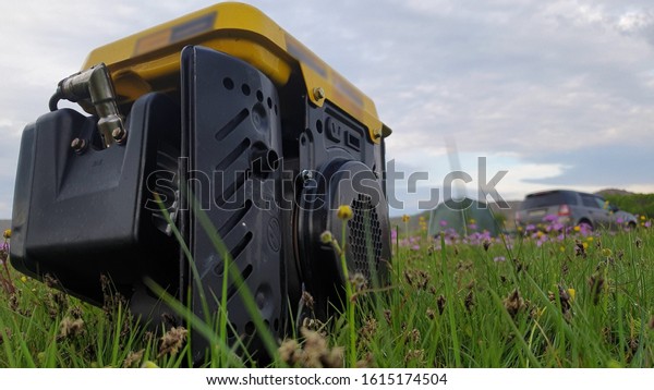 Close up of gas diesel mobile portable\
electricity generator work on grass. Gasoline fuel powered portable\
generator give electric energy current for camping. Background:\
grass, tent, car.\
Outdoor.