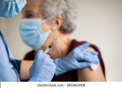 Cierre de la aplicación de la vacuna de la mano del médico general mientras lleva una máscara protectora facial durante la pandemia de covid-19. Enfermera joven con máscara quirúrgica inyectando a la anciana.