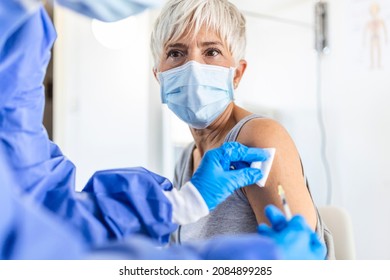 Close up of general practitioner hand holding vaccine injection while wearing face protective mask during covid-19 pandemic. Young woman nurse with surgical mask giving injection to senior woman.
