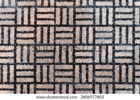 Close up of geometric patterned carpet with repeating square and line design in neutral tones.