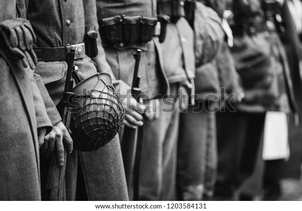 Close Up Of German Military Ammunition Of A German
Soldier. Unidentified Re-enactors Dressed As World War II German
Soldiers Standing Order. Photo In Black And White Colors. Soldiers
Holding Weapon 
