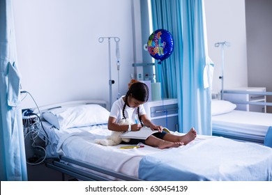 Close up of girl drawing picture in a book while sitting on hospital bed  - Powered by Shutterstock