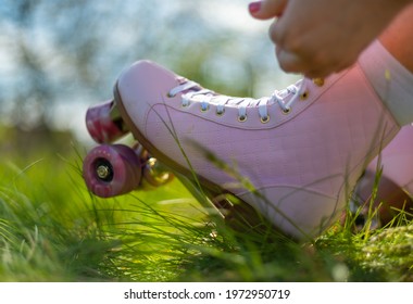 Close Up Girl Puts On Pink Vintage Quad Roller Skates On Grass In Park. Concept: Summer, Sports, Vacations, Free Time, Outdoor Activities.