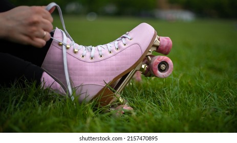 Close Up Girl Puts On Pink Vintage Quad Roller Skates On Grass In Park. Concept: Summer, Sports, Vacations, Free Time, Outdoor Activities.