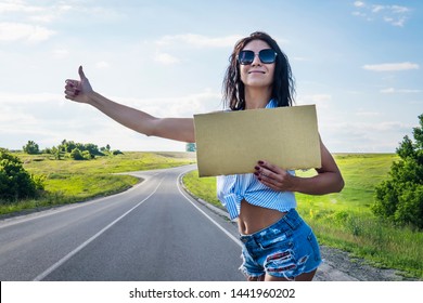 Close up girl travels hitchhiking with a cardboard sign in her hands. Space for text. a girl in glasses shorts and heels road on roadside holding a empty plate and catches the car. thumb up to go