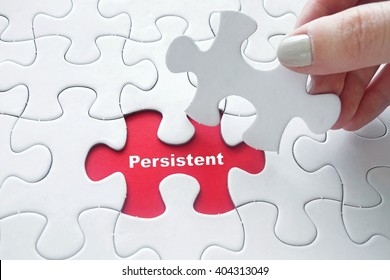 Close up of girl's hand placing the last jigsaw puzzle piece with word Persistent as personality concept