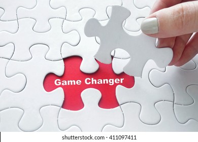 Close Up Of Girl's Hand Placing The Last Jigsaw Puzzle Piece With Word Game Changer As Business Concept