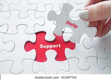 Close up of girl's hand placing the last jigsaw puzzle piece with word Help and Support as business concept