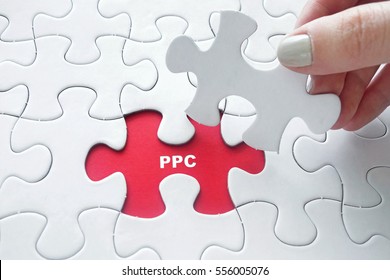 Close up of girl's hand placing the last jigsaw puzzle piece with word PPC ( Pay Per Click )
