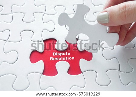 Close up of girl's hand placing the last jigsaw puzzle piece with word Dispute Resolution