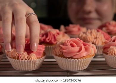 Close up of a girls hand stealing a pink iced frosted cupcake
