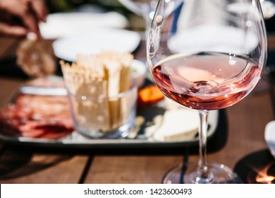 Close up of a glass of wine and a plate of crackers and meat on a sunny day