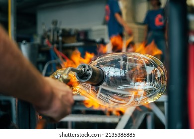 Close up of a glassblower artisan shaping the hot molten glass at strong fire inside a workshop. Manual glass processing by the craftsmen inside a glass factory - Powered by Shutterstock