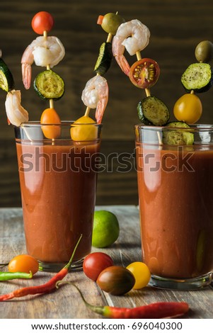 Close up of glasses with bloody mary cocktail and shrimp, cherry tomatoes, olive, grilled zucchini on skewers.