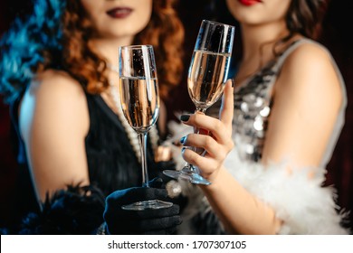 Close up glasses of champagne. Flappers women wearing in style of Roaring Gatsby twenties drinking alcohol. Vintage, retro party, fashion, girls friends concept