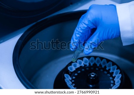Close up of a gloved hand placing sample tubes into a laboratory centrifuge. The image represents science, biotechnology, research, and laboratory equipment.