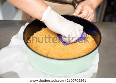 Close up of gloved hands pressing cookie crumbs into a springform pan, creating the base for a delicious dessert