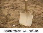 Close up of gold painted shovel head dug into sand and rock dirt at ceremonial ground breaking event for commercial and residential building development