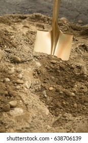 Close Up Of Gold Painted Shovel Head Dug Into Sand And Rock Dirt At Ceremonial Ground Breaking Event For Commercial And Residential Building Development