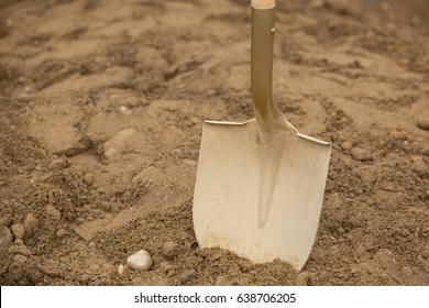 Close Up Of Gold Painted Shovel Head Dug Into Sand And Rock Dirt At Ceremonial Ground Breaking Event For Commercial And Residential Building Development