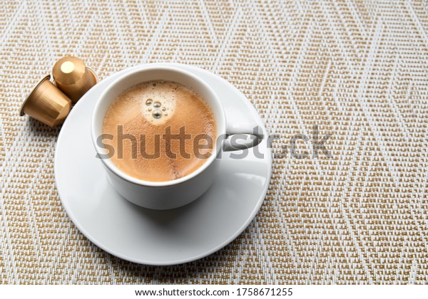 Close up golden capsules or pods for\
coffee mashine with cup on gold and white background.\
