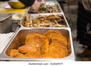 Close Up Of Golden Fried Patties Keeping Warm In Hot Steamer Dish In Long Line Of Buffet At Outdoor Food Festival With Customers Serving Selves In Background