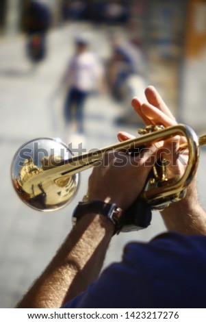 Close up of golden trumpet in hands playing street music. Shiny trumpet with reflection of architecture. Outdoor on sunny day. Vivid fingers of a musician holding instrument and playing music for tip