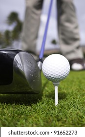 Close up of a golfer's driver with a blue shaft, ball and tee setup.