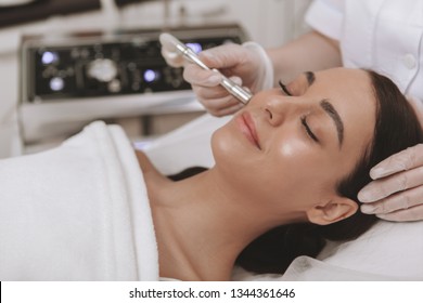 Close up of a gorgeousyoung woman with perfect glowing healthy skin receiving microdermabrasion facial treatment by professional cosmetologist. Beautician cleaning skin of a woman