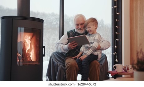 Close up grandfather and grandson using digital tablet for surfing internet and playing game near the fireplace at home grandpa adult grandchild child childhood communication computer slow motion