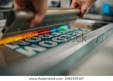 Close up of graphic worker's hands using rubber blade and pressing ink while silkscreen printing at printing workshop. Cropped picture of graphic worker's hands using squeegee for silkscreen printing.