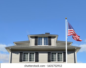 Close Up Of Gray Suburban Home With American Flag Blue Sky Clouds Sunny Day