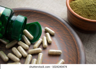 Close up Green capsules, bottle and powder on a clay brown plate on a burlap background. Dietary supplements for Weight Loss and detox. vitamins and minerals for vegans and vegetarians. Superfood