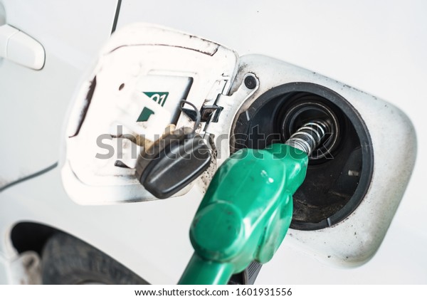 Close up of green gas refueling gun refueling\
gas into a white car at a gas\
station