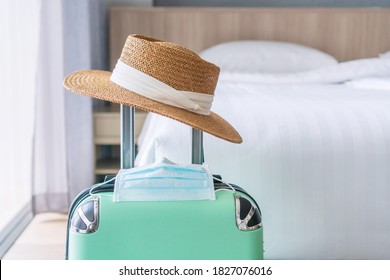 Close up of green luggage, straw hat and surgical mask. Hotel room bed background, copy space for text, Traveling in new normal lifestyle concept.