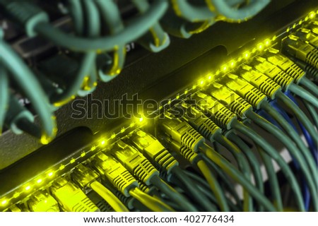  Close up of green network cables from data center connected with patch cord to black switch glowing in the dark. Blurred frame vignetting 