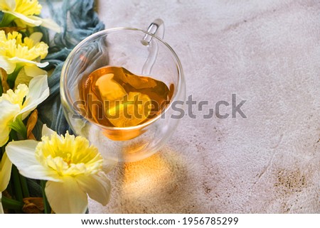 Close up of Green tea in a in a heart-shaped glass cup with a double bottom on the napkin with daffodil flowers on the table. Spring still life.