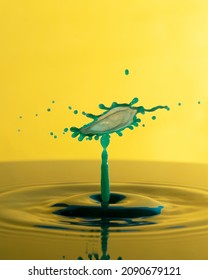 Close up of green water drops collision on a yellow background. Splash of water crown on the surface.