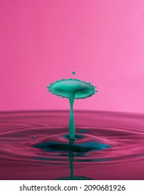 Close up of green water drops collision on a pink background. Splash of water crown on the surface.
