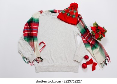 Close up grey blank template sweatshirt copy space. Christmas Holiday concept. Top view mockup hoodie, scarf, hat. Red holidays decorations on white background. Happy New Year accessories. Xmas outfit