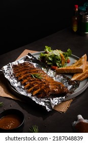 Close Up Grilled Bbq Ribs On Aluminium Foil In Grey Circle Ceramic Plate With Toast On Black Table