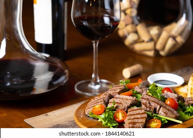 close up of grilled beef tenderloin fillet with rocket salad and cherry tomatoes pairing with Italian fine red wine bottle, glass and decanter in a wooden table classic vintage elegant moody style