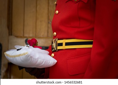 Close Up Of Groom In Red Rcmp Uniform Holding Wedding Rings On A Pillow Showing Only Their Midsection And Displaying Rings Before The Wedding Ceremony