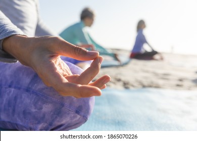 Close up of a group of Caucasian female friends enjoying exercising on a beach on a sunny day, practicing yoga, meditating in lotus position. - Powered by Shutterstock